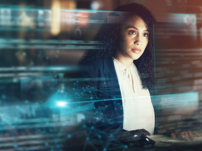 A woman in a blazer working on a computer with digital overlays.