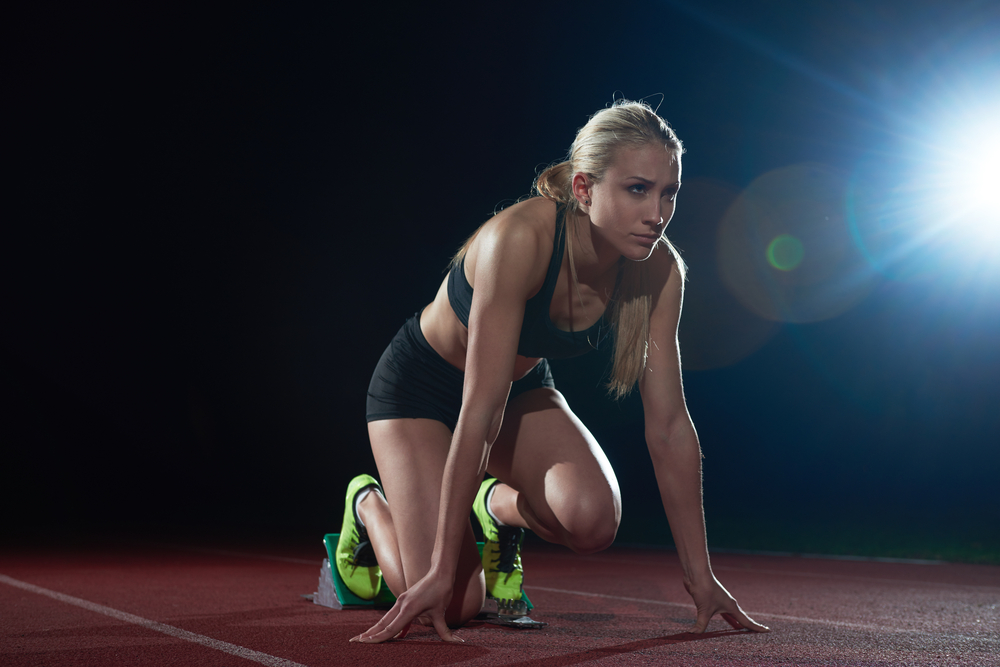 woman  sprinter leaving starting blocks on the athletic  track. Side view. exploding start