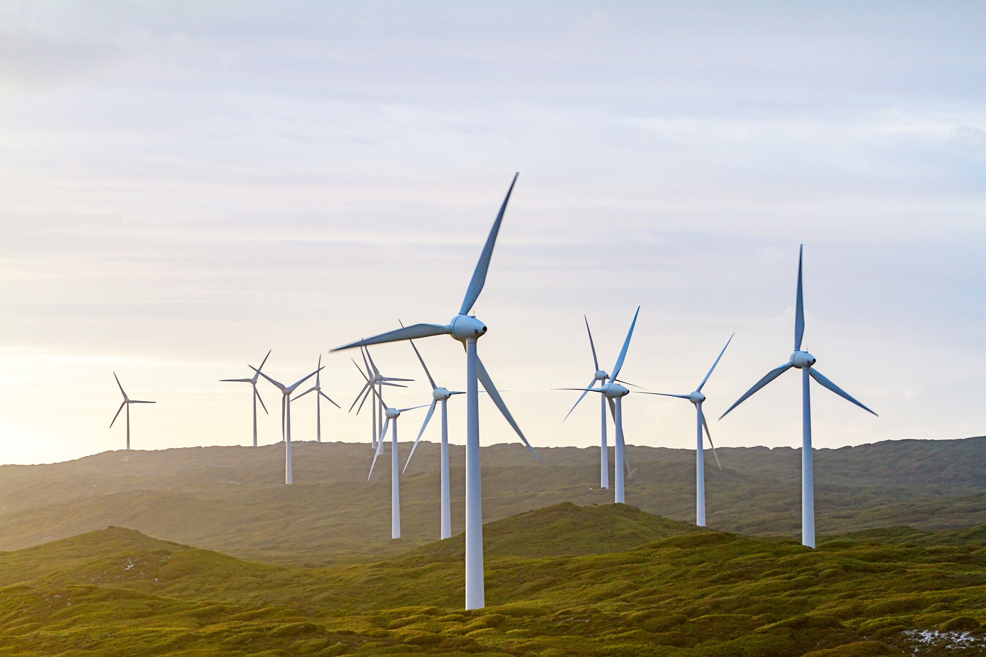 A row of wind turbines on a grassy hill during daylight, generating renewable energy A row of wind turbines on a grassy hill during daylight, generating renewable energy